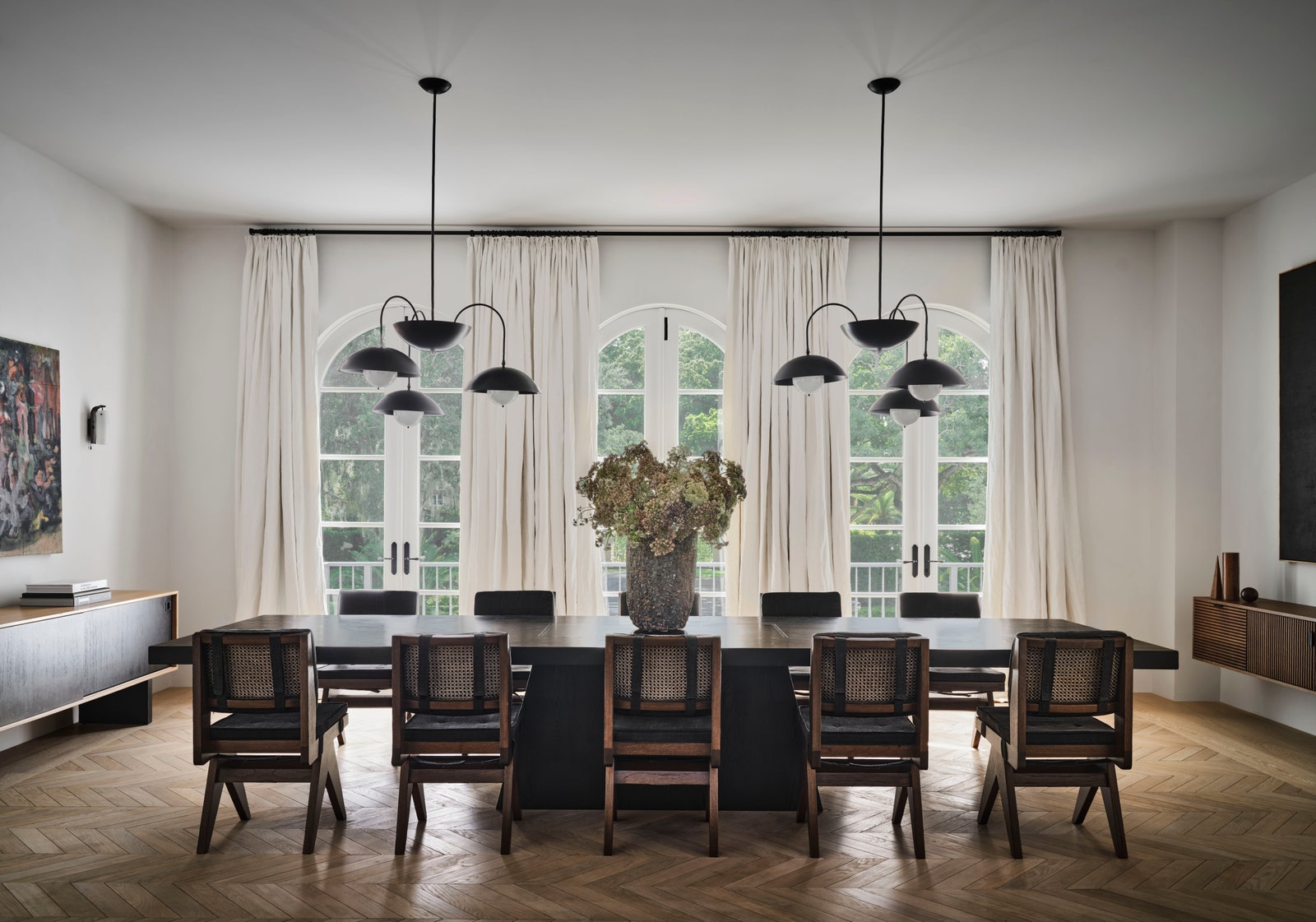 Dining room with long dining table five chairs on each side three arched french doors two pendant lights overhead