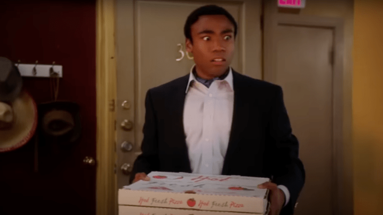 Troy Barnes (Donald Glover) holding a pizza with a horrified expression in Community "Remedial Chaos Theory."